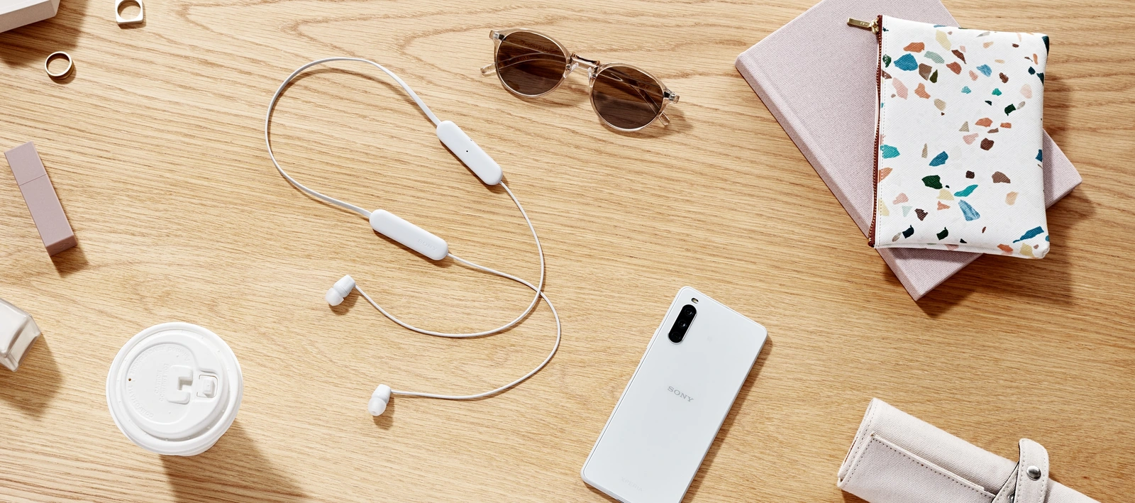 Бездротові навушники Sony WI-C100 білого кольору на столі поруч зі смартфоном Xperia й окулярами