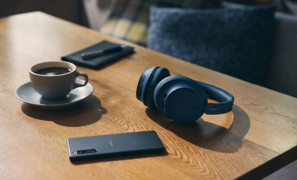 Беспроводные наушники Sony WH-CH720N чёрного цвета на столе возле смартфона Xperia и чашки кофе