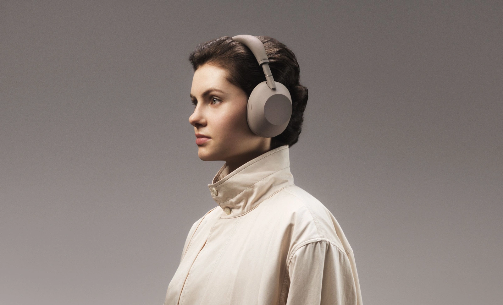 Девушка в бежевой куртке с высоким воротником в наушниках Sony WH-1000XM6, вид сбоку