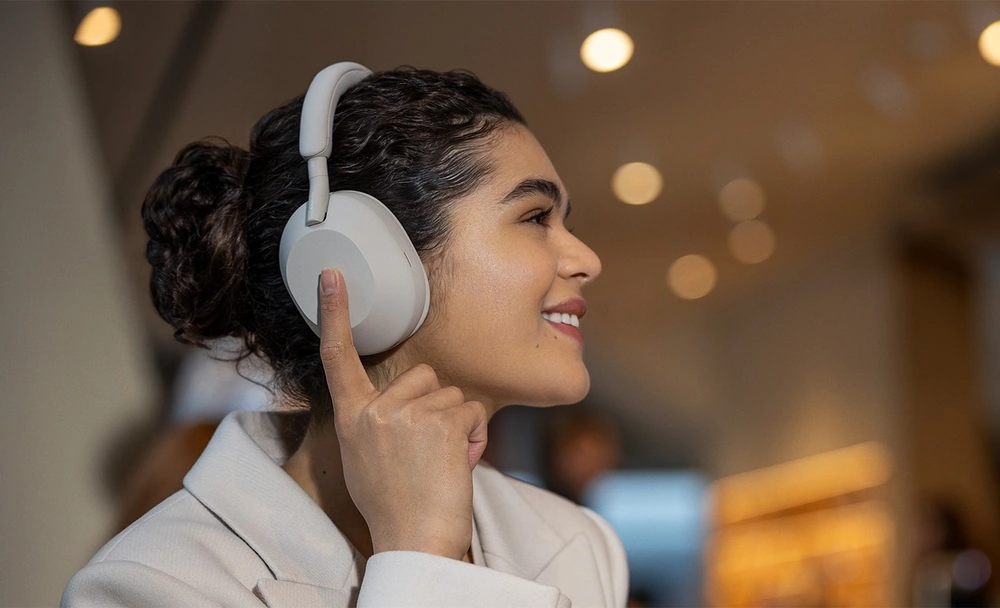 Девушка прикасается к сенсорной панели на чашке наушников Sony WH-1000XM5