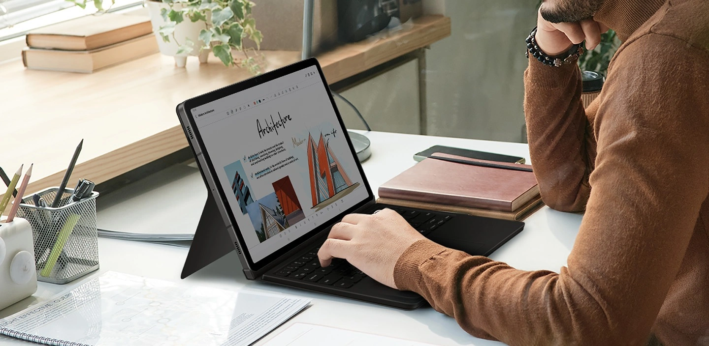 Чоловік використовує планшет Galaxy Tab S9, тримаючи руку на обкладинці-клавіатурі Book Cover Keyboard.